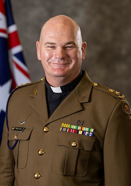 Fr Damian STyles in his official Military uniform with Australian flag in the background