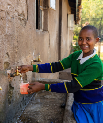 Young African girl pouring water out of a tap on a wall outside during the day