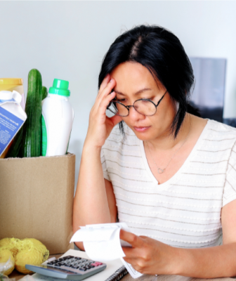 Mother leading head against hand reading through bills after groceries shopping at the table inside her home
